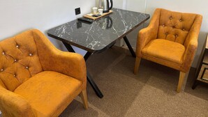Quarto com mesa de mármore preto, duas poltronas estofadas em tom de mostarda, uma cafeteira e um suporte com xícaras e um controle remoto.