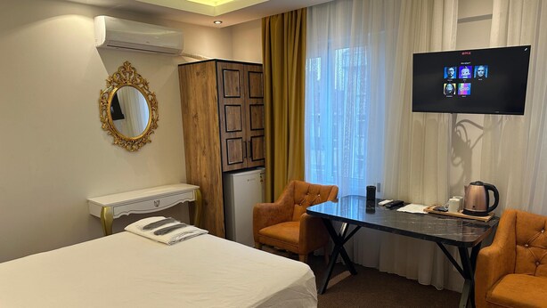 A hotel room with a bed, a desk, two chairs, a television, and a minibar. - Ananas Suite (Istanbul)