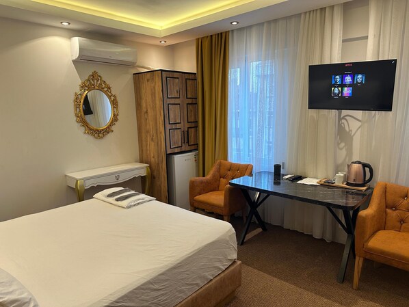 Une chambre d’hôtel équipée d’un lit, d’un bureau, de deux chaises, d’une télévision et d’un mini-bar.