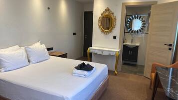 A hotel room with a large bed, a bedside table, a mirror, a vanity with a sink, and a door leading to another room.