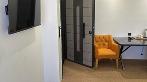 Quarto moderno com televisão de tela plana na parede, divisória com porta deslizante, poltrona laranja com estofamento e mesa com controle remoto.