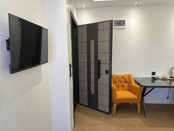 Une chambre moderne dotée d’un téléviseur à écran plat fixé au mur, d’une cloison avec une porte coulissante, d’un fauteuil orange à motifs et d’une table avec une télécommande.