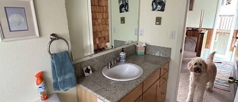 A bathroom with a toilet, sink, and mirror. There is a towel rack, a picture frame, and a small bottle on the counter.