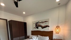 A spacious bedroom with a large bed, a ceiling fan, a wall-mounted artwork, and a bedside table with a lamp.