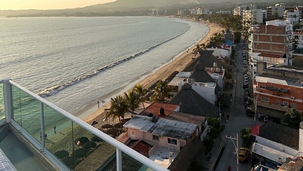 A coastal cityscape with a beach, buildings, and mountains in the background.