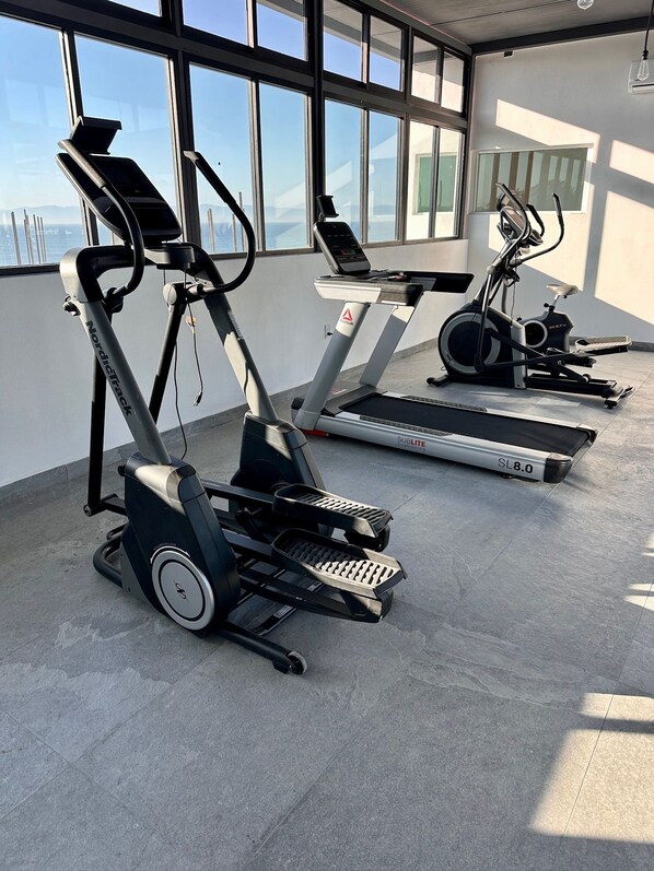 Une salle de sport équipée de tapis de course et d’appareils elliptiques, dotée de grandes fenêtres et arborant un design moderne.