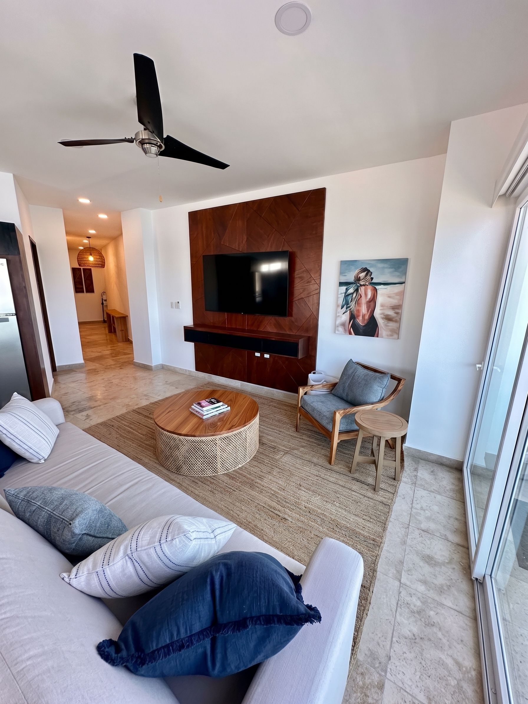 A modern living room with a flat-screen TV, a ceiling fan, a sofa with cushions, a coffee table, and a painting on the wall.