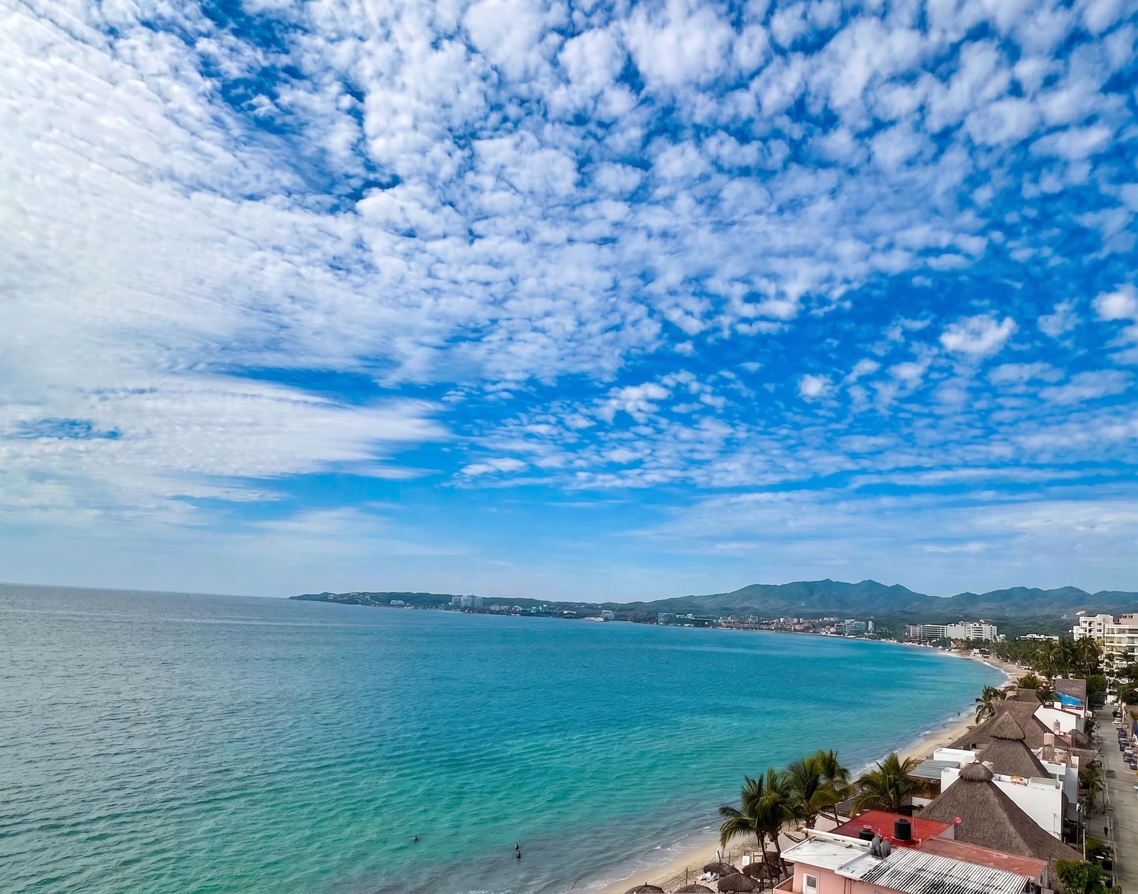 A coastal view with a beach, clear sky, and distant mountains.