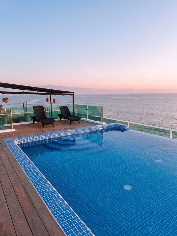 A swimming pool with a wooden deck and lounge chairs, overlooking a body of water. - NEW Oceanfront in Heart of Bucerias! (Bucerías)