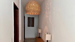 A hallway with a woven ceiling light fixture, a bench, two wall-mounted lamps, and a door at the end.
