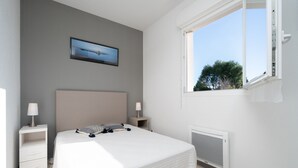 Un dormitorio con cama, dos mesitas de noche, ventana, radiador y un cuadro en la pared.