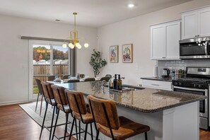 Uma cozinha com ilha central, banquetas, eletrodomésticos de aço inoxidável e uma janela grande.