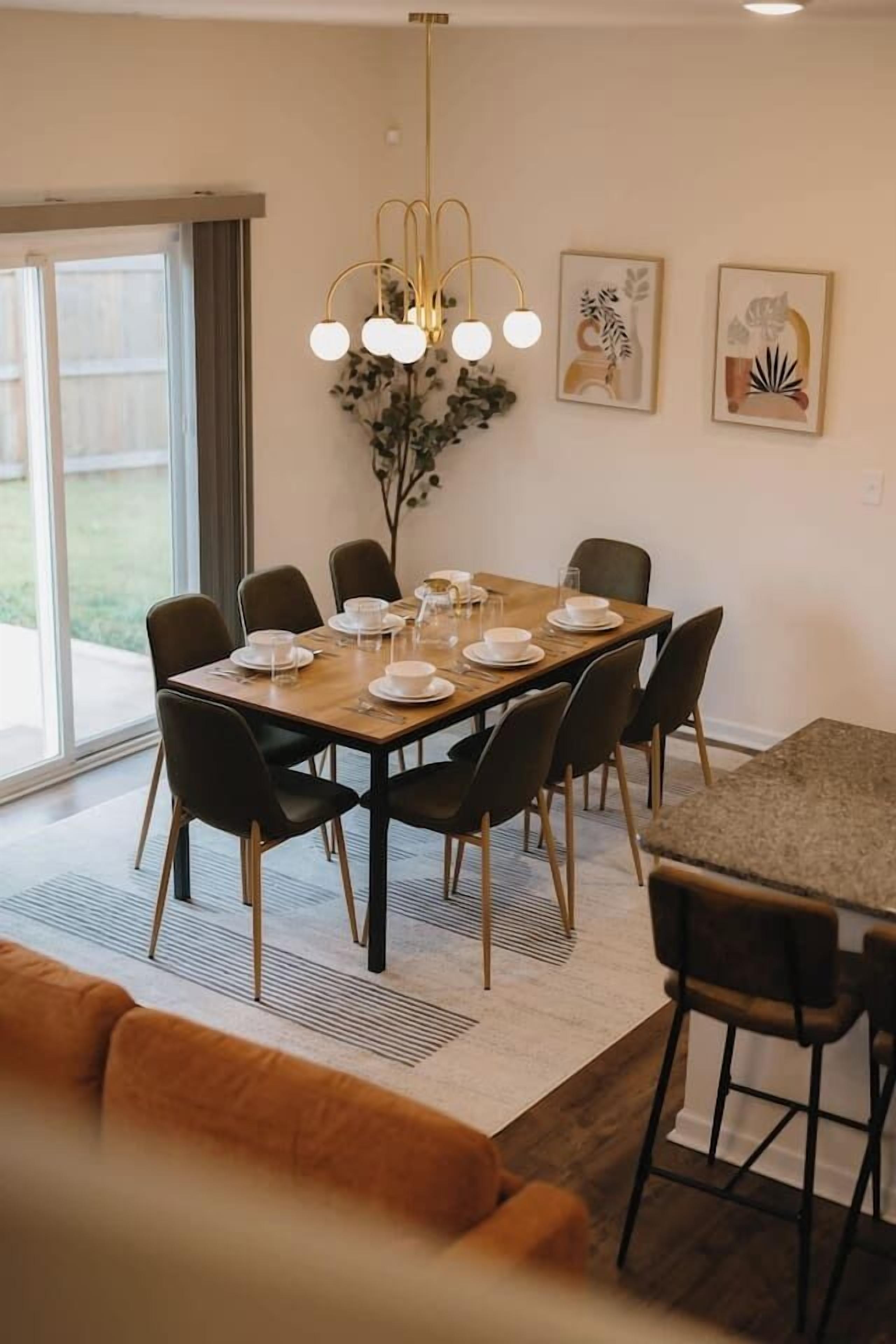 A dining area with a table set for six, chairs, a chandelier, and artwork on the wall.