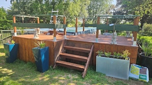 Eine Holzterrasse mit Metall-Pergola, Treppen und Pflanzkübeln.