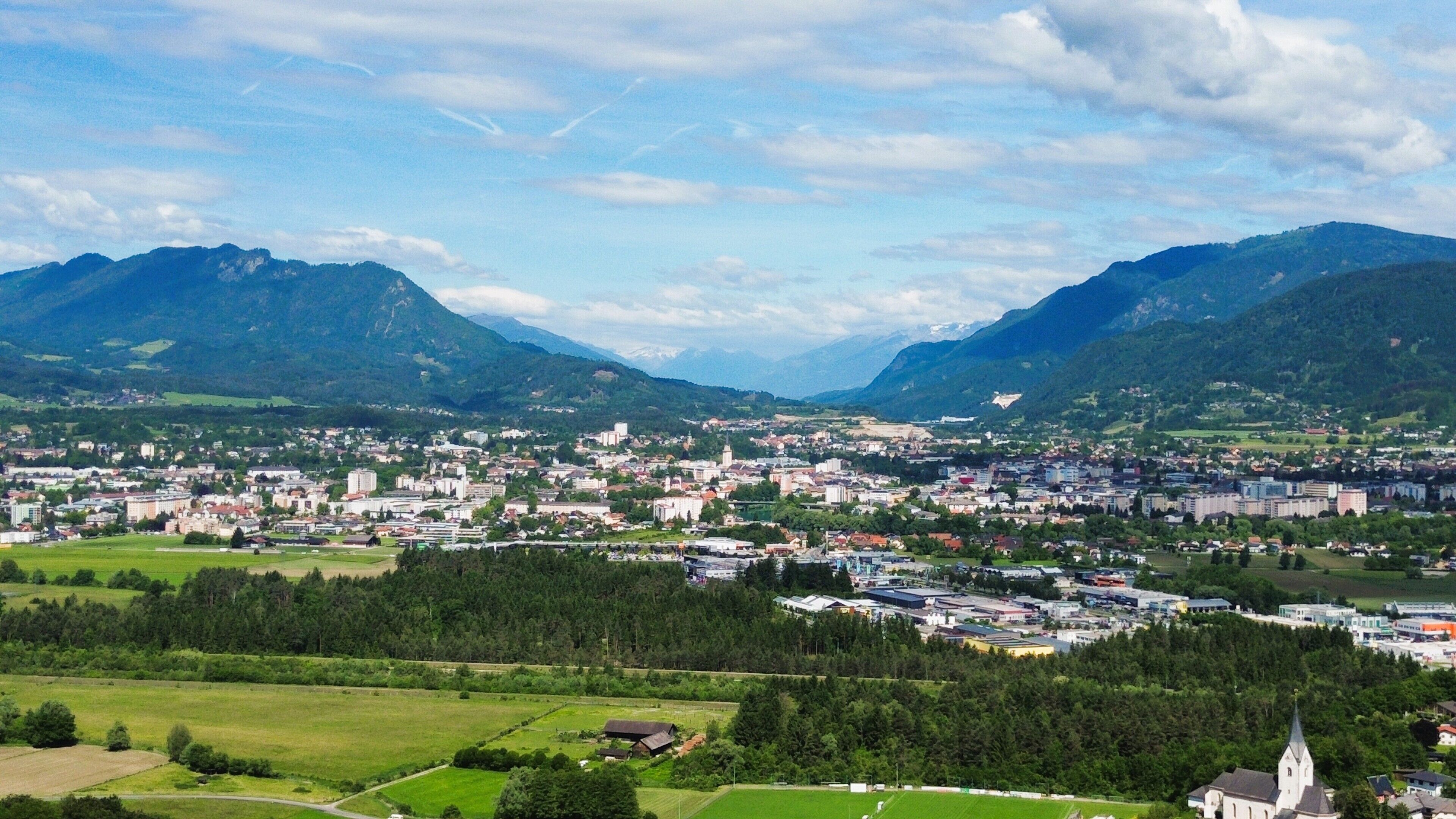 A town nestled between mountains with a mix of residential and commercial buildings, surrounded by green fields and a church.