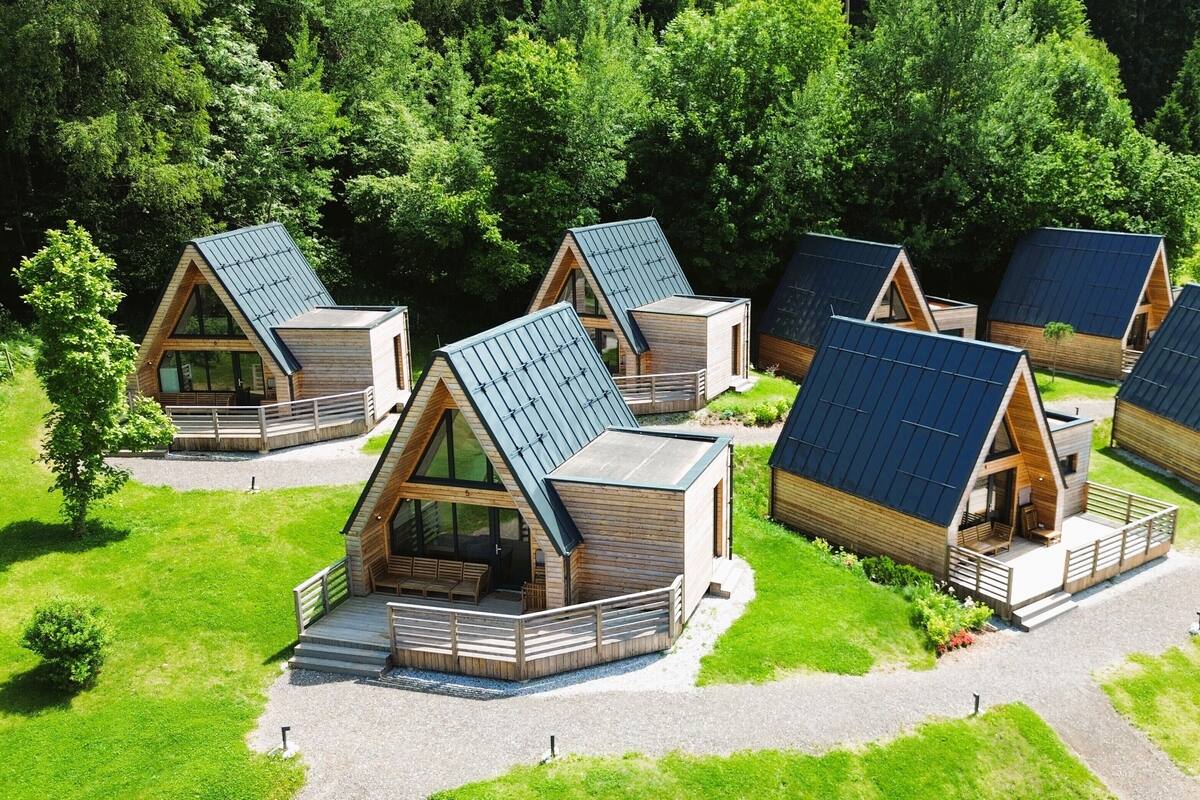 Un ensemble de chalets modernes à toit en forme de « A », dotés de panneaux solaires, et entourés d’une végétation luxuriante.
