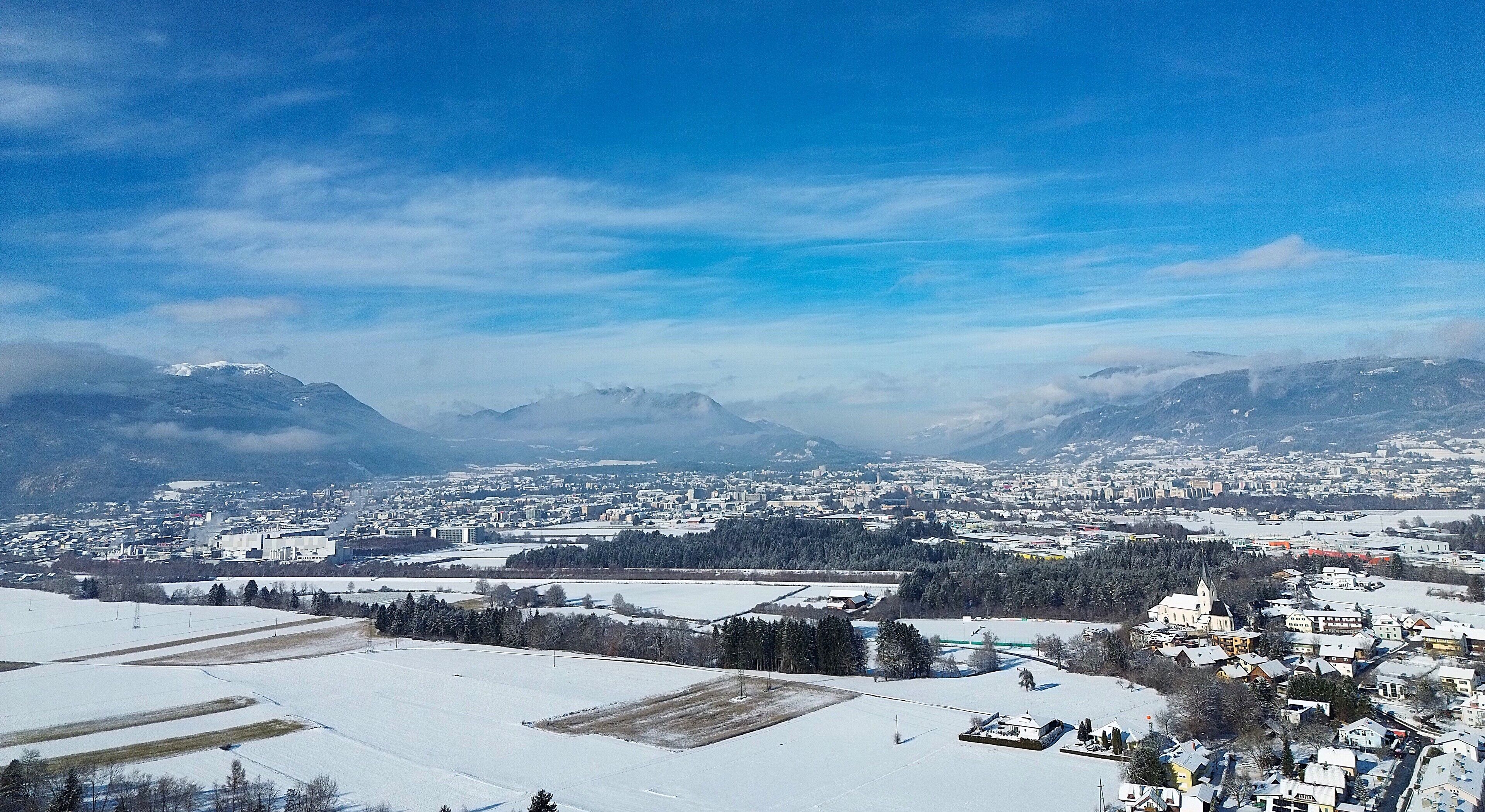 A panoramic view of a town with snow-covered fields, buildings, and mountains in the background.