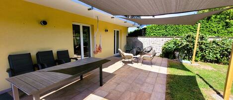 An outdoor patio with a long table and several chairs, a hanging chair, and a covered area with a canopy.