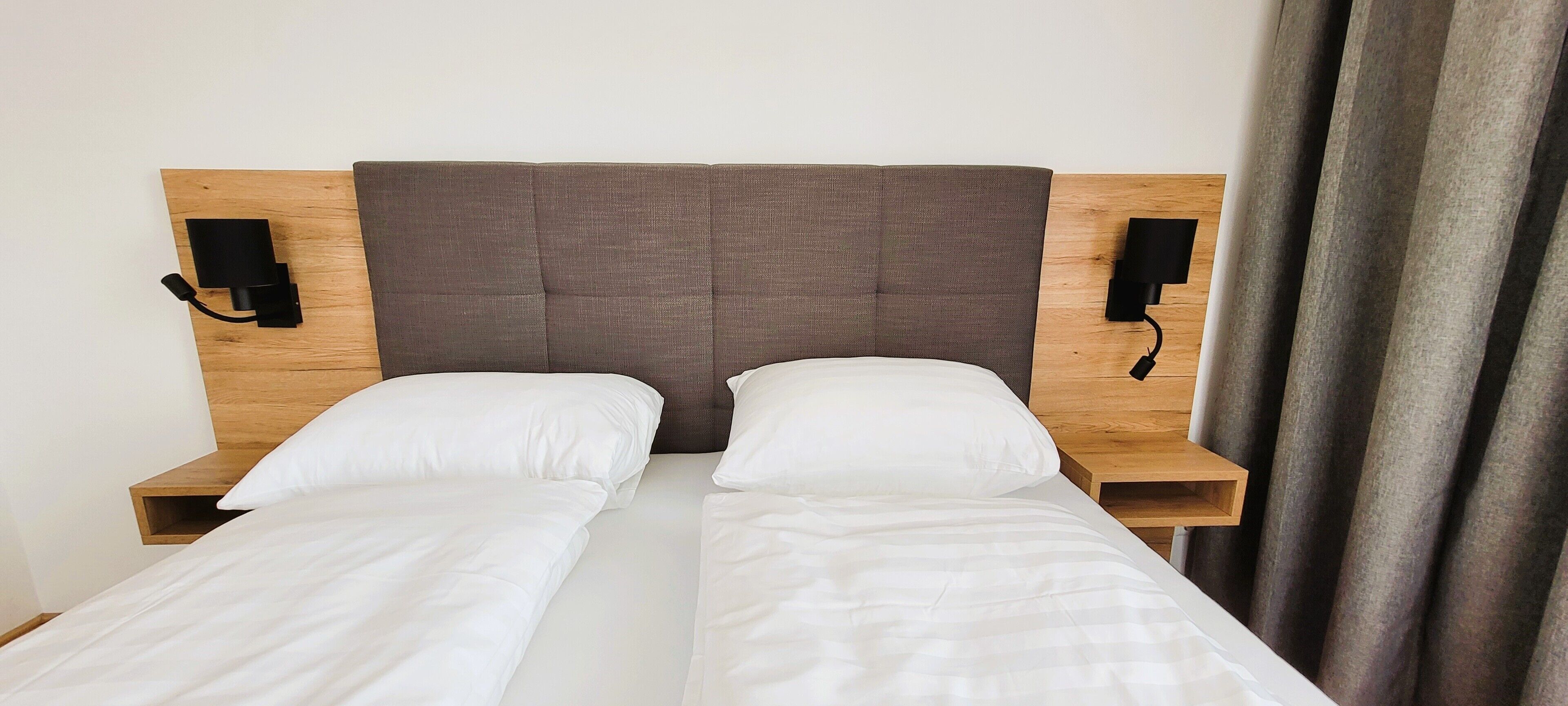 Un lit double avec une tête de lit en bois et deux tables de chevet, chacune équipée d’une lampe.