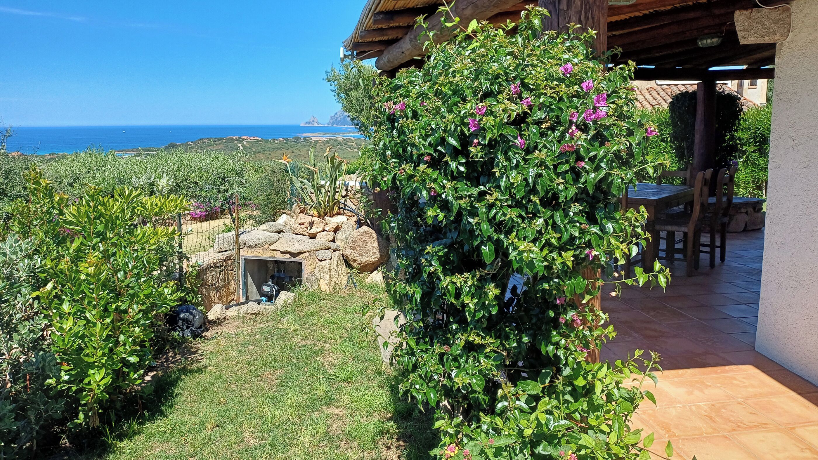 Un jardin avec un mur en pierre, une table en bois et une vue sur l’océan.