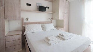 A neatly arranged bedroom with a bed, bedside tables, a TV on a shelf, and a wardrobe. - Profumo di Mare - Two Bedroom Apartment, Sleeps 4 (Olbia)
