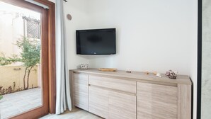 Un salon moderne avec un téléviseur à écran plat fixé au mur, un meuble en bois agrémenté d’objets décoratifs et une porte-fenêtre coulissante donnant sur un espace extérieur.