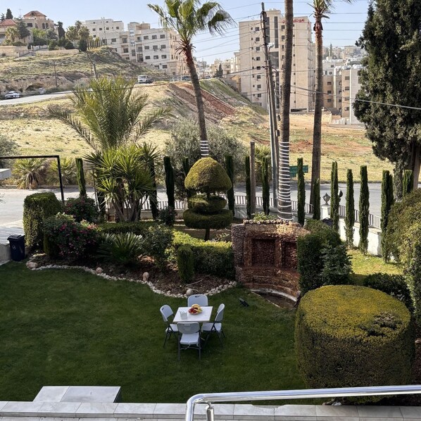 A well-maintained garden with a dining area, neatly trimmed hedges, and a view of the surrounding urban landscape.
