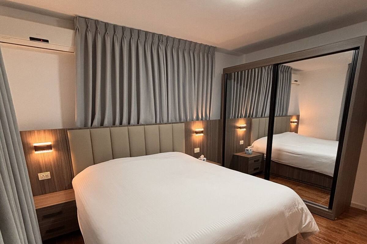 A modern hotel room with a large bed, a mirror, and a wooden floor.