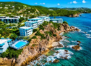 Un hotel frente al mar con varias construcciones, piscina y acantilados rocosos.