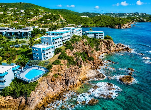 A coastal hotel with multiple buildings, a swimming pool, and rocky cliffs.
