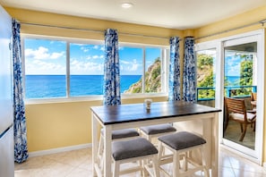 A room with a dining table, two chairs, a view of the ocean, and a sliding glass door leading to an outdoor area.