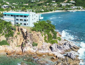 A coastal property with a large building overlooking the ocean, featuring a rocky cliff and clear blue waters.