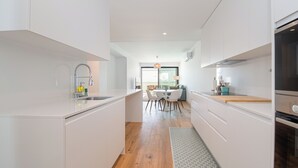 Une cuisine moderne avec des meubles blancs, un îlot central et un coin repas comprenant une table et des chaises.