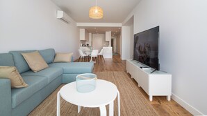 Un salon moderne avec un canapé, une table basse, un téléviseur posé sur un meuble et, au fond, un coin repas.