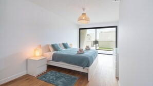 Une chambre moderne avec un lit, une table de chevet et une vue à travers une porte vitrée.