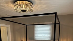 Een hemelbed, twee nachtkastjes met lampen, een groot raam met jaloezieën en een geweven vloerkleed.