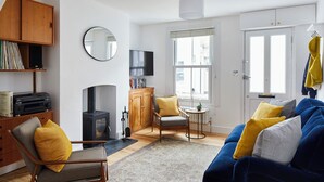A living room with a sofa, a chair, a wooden cabinet, a television, a fireplace, and a window.
