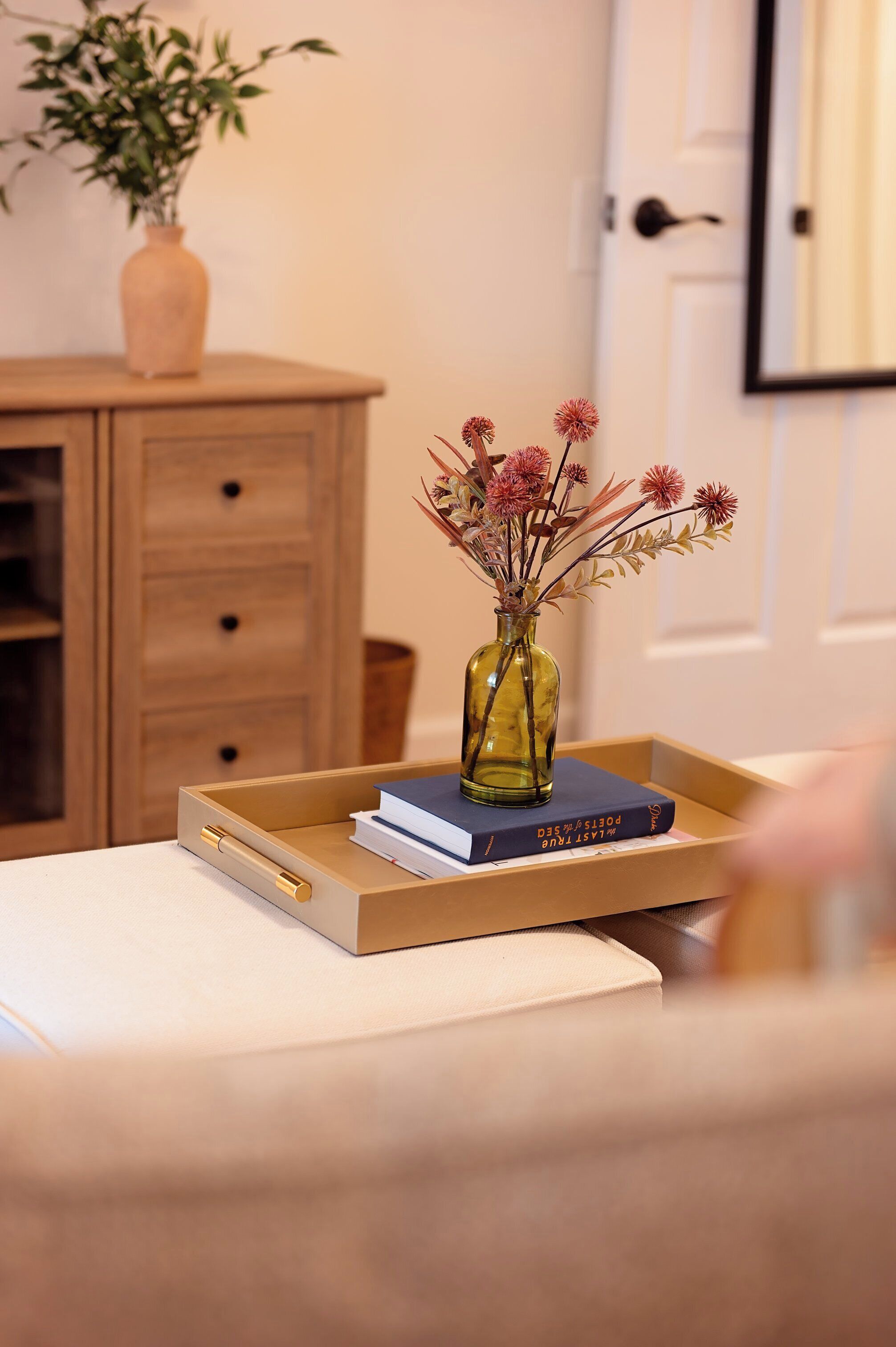 Een houten dressoir met een vaas gedroogde bloemen en boeken erop.