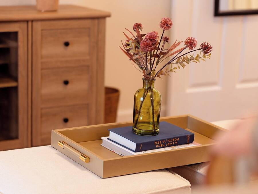 Een houten dressoir met een vaas gedroogde bloemen en boeken erop.