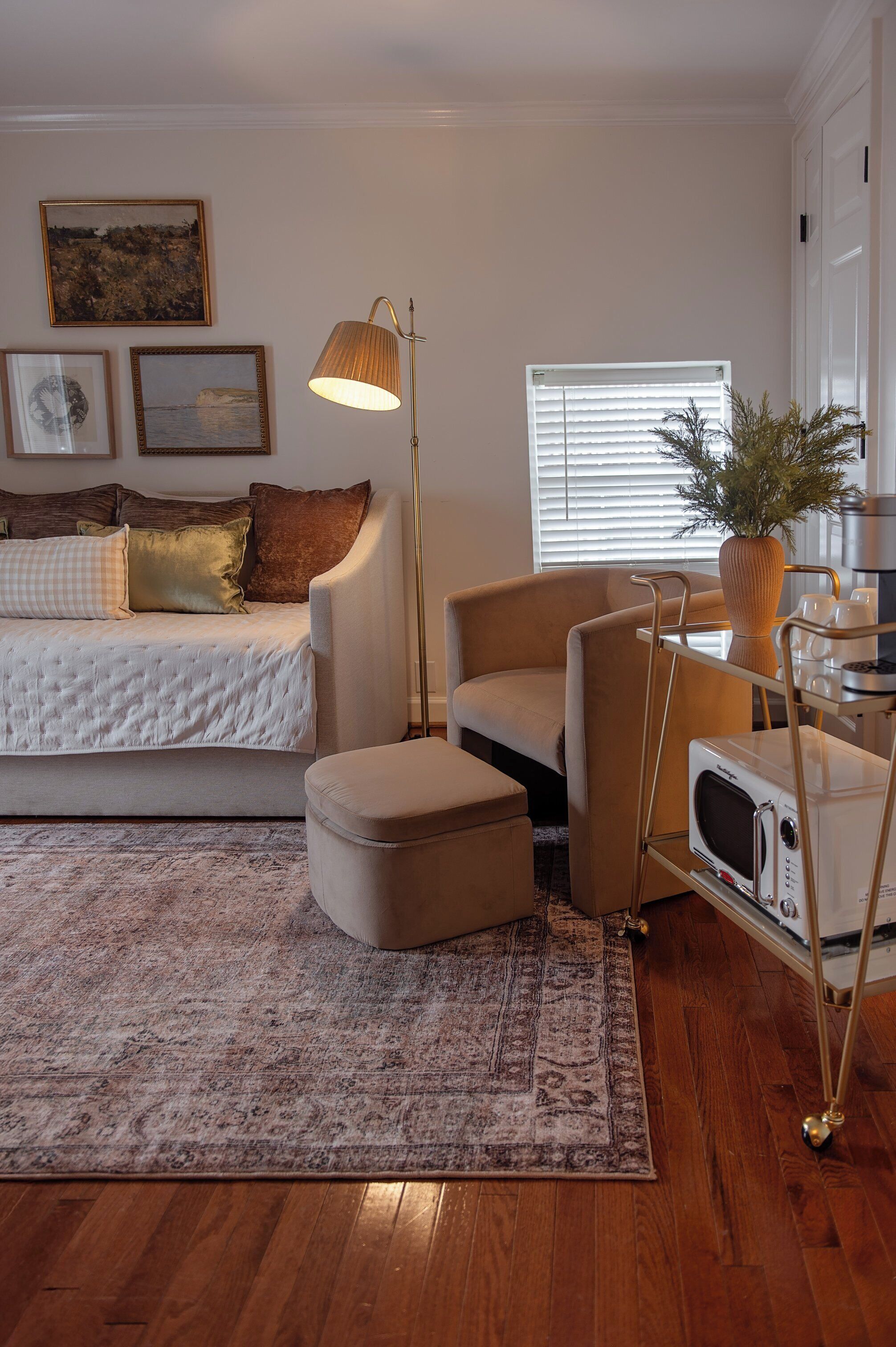A modern living room with a sofa, armchair, ottoman, floor lamp, and a microwave on a cart.