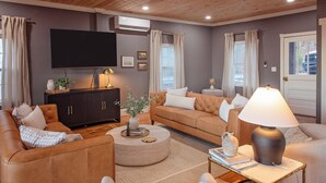 A modern living room with a flat-screen TV, a dark wooden cabinet, a round coffee table, and a beige sofa.