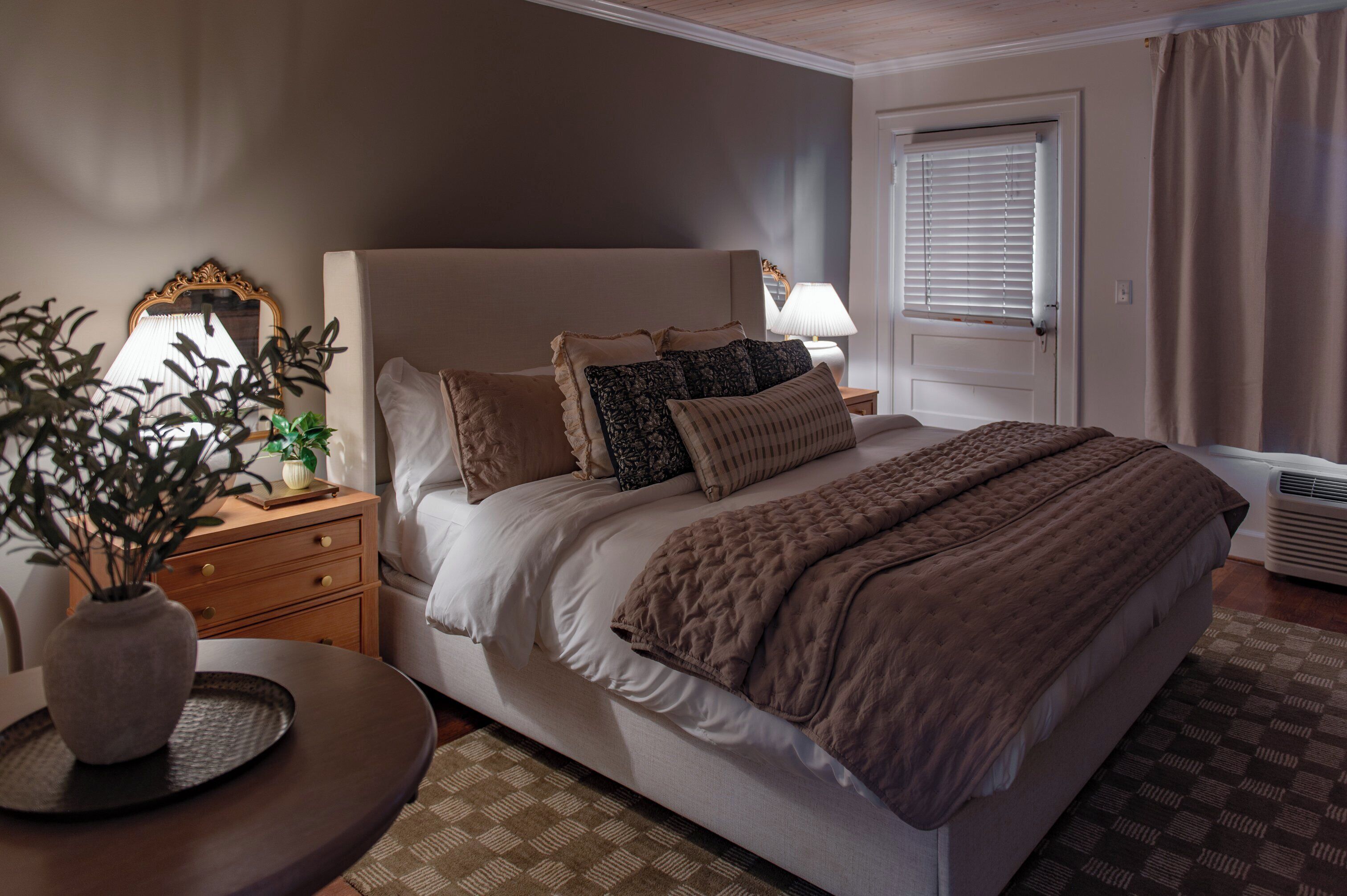 Une chambre bien rangée, avec un grand lit, des tables de chevet, une lampe et une plante en pot.