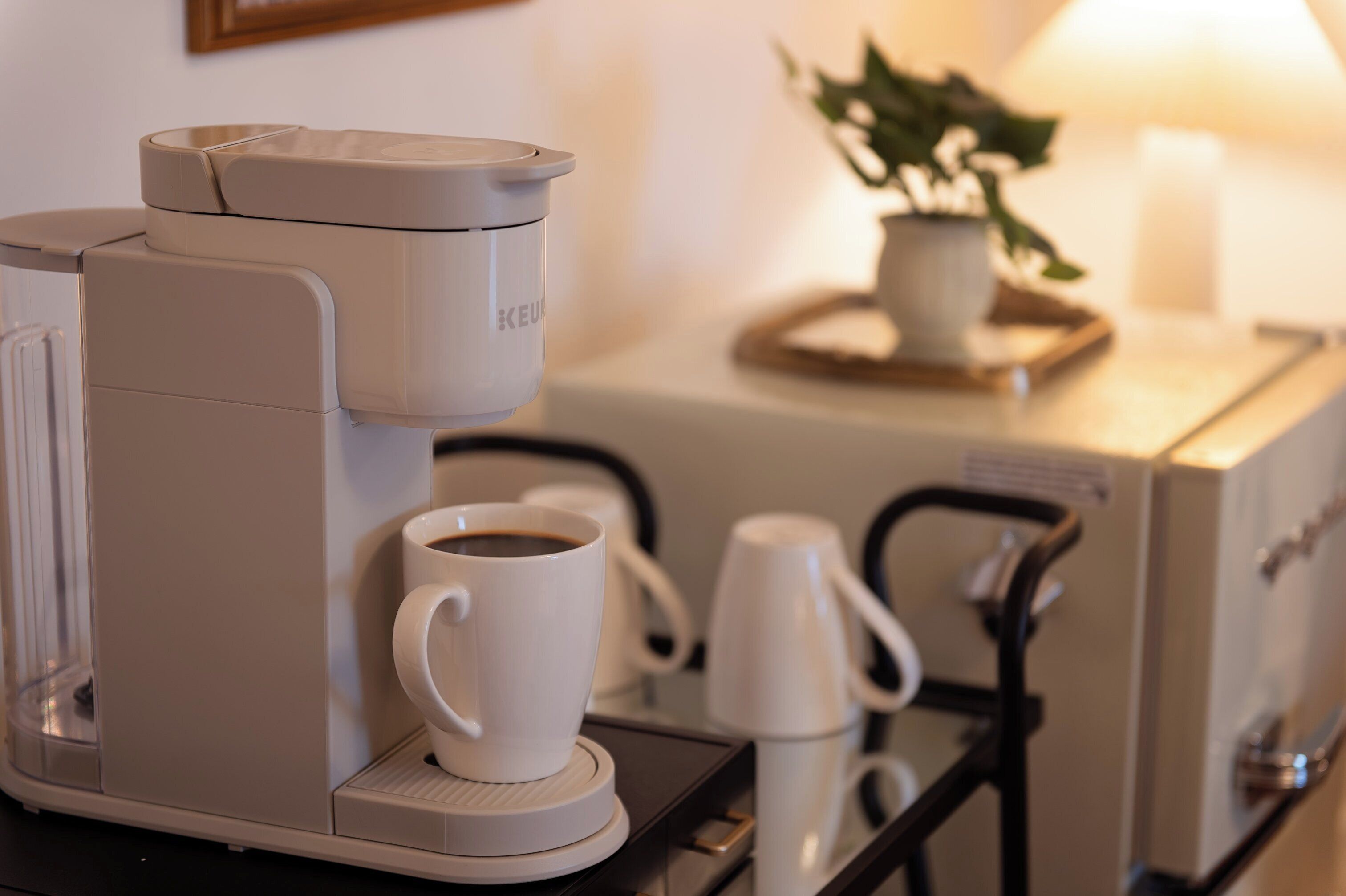 Una cafetera con una taza de café sobre una bandeja, una taza blanca y una máquina de café en una mesa.