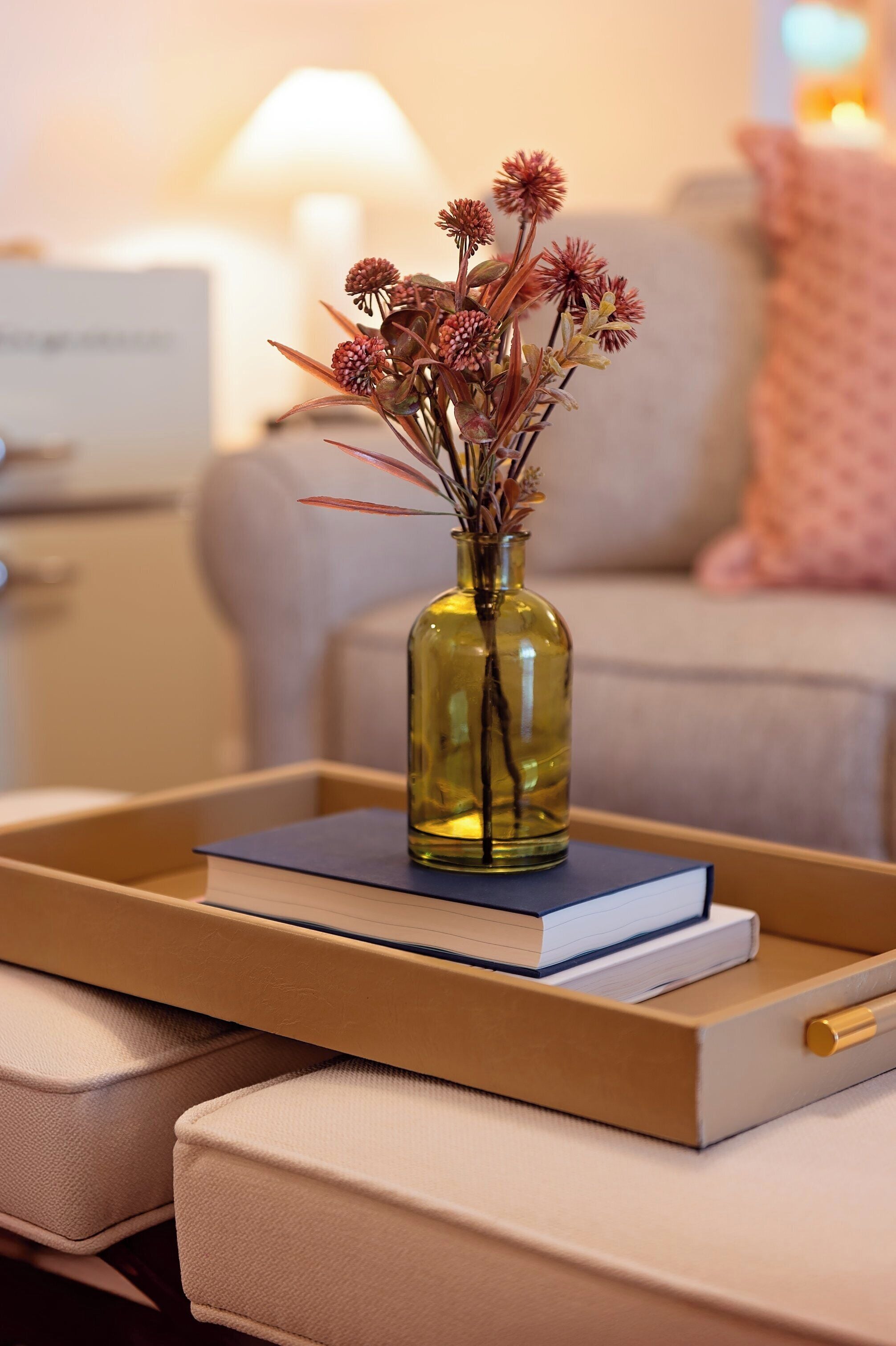 A vase with dried flowers on a tray, placed on a couch with a book beside it.