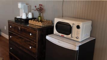 A microwave oven on top of a refrigerator, a coffee maker, and a vase with flowers on a wooden dresser.
