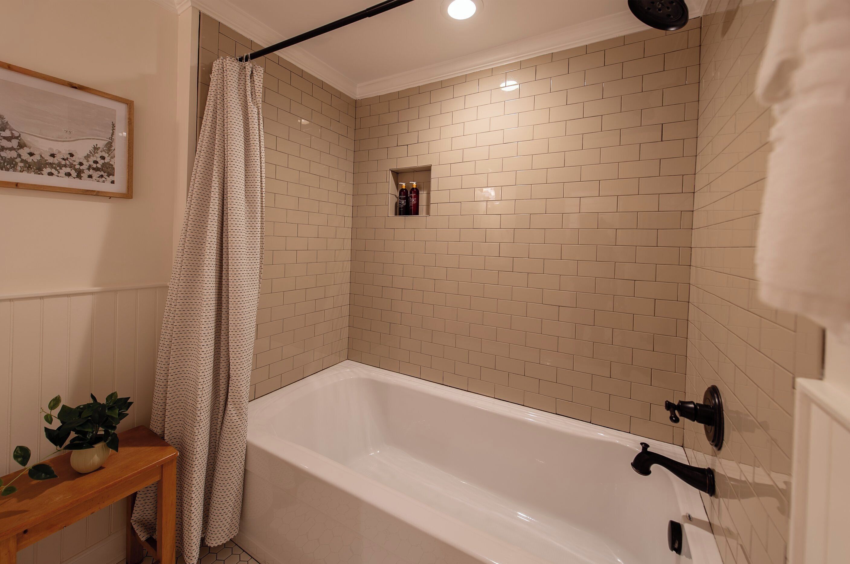 Ein Badezimmer mit einer Badewanne, einer Duschvorhang, einem kleinen Ablagefach für Toilettenartikel und einem gerahmten Bild an der Wand.