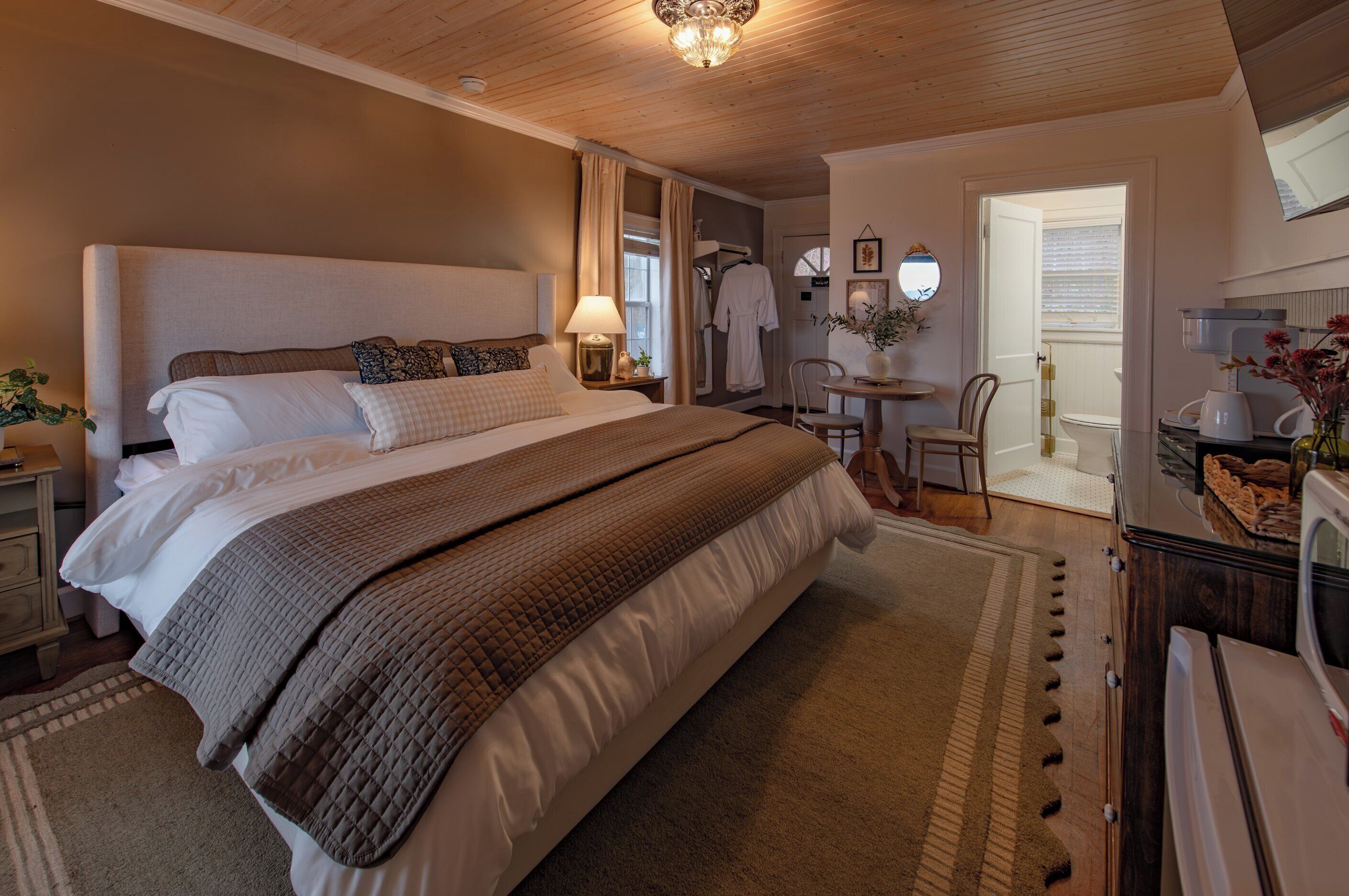 Une chambre à coucher avec un grand lit, des tables de chevet, une lampe, une chaise, une petite table et un miroir.