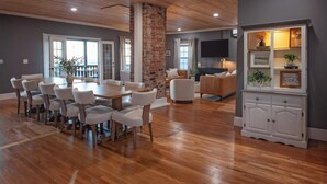 A spacious living area with a wooden dining table and chairs, a brick accent wall, a cozy seating area with a sofa and armchairs, and a cabinet with decorative items.