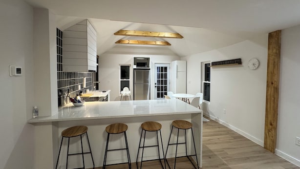 A modern kitchen with a central island, bar stools, and a wooden ceiling beam.