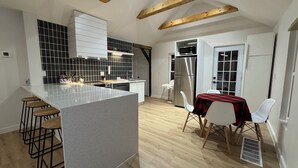 A modern kitchen with a central island, wooden beams, and a dining area with a table and chairs.